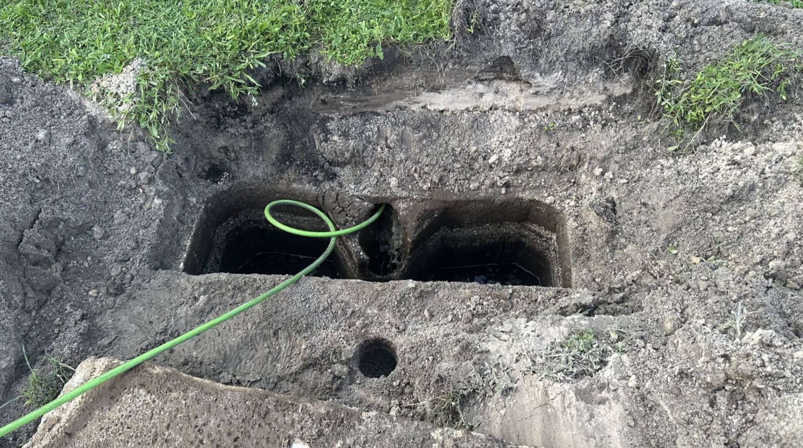 An opened two-chamber concrete septic tank with the suction hose feeding into it.